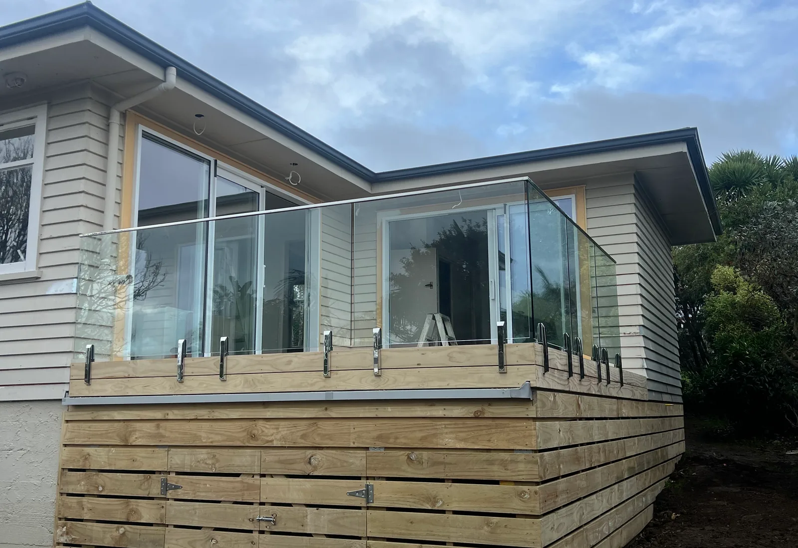 A glass-balustrade fence around a Raglan deck, sitting on a horizontal timber base wall